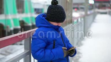 穿着蓝色羽绒服的男孩在街上读信息智能手机。